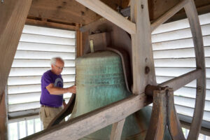 Man patting large church bell in bell tower.