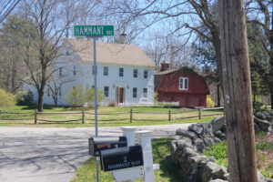 White two story house with red barn to right with mailboxes in front of stone wall