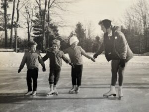 Mother with three young girls on ice skates on frozen pond