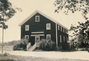 Dark two story building with white trim and white stairs leading to door