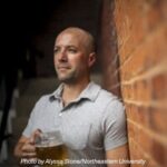 Man leaning against brick wall holding a mug of beer