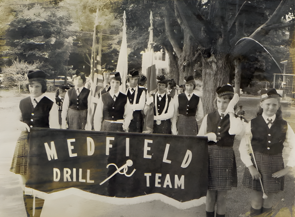 Young women dressed in tartan plaid carrying Medfield High School banner