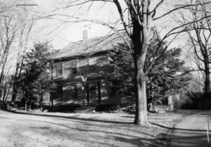 Black and white picture of a colonial house shaded by a large tree